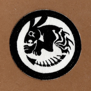 以下が含まれることがあります： 円の中にスタイリッシュなウサギが描かれた、黒と白の刺繍パッチです。