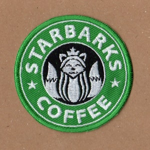Puede incluir: Parche bordado verde con el texto "STARBARKS COFFEE" en blanco y una imagen estilizada en blanco y negro de un zorro con una corona en el centro.
