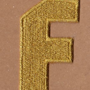 May include: A gold embroidered letter F patch. The patch is made of a soft, textured fabric and has a slightly frayed edge.