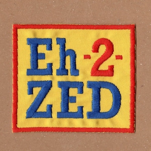 May include: A yellow fabric patch with a red border. The patch has blue embroidered text that reads "Eh-2-ZED".