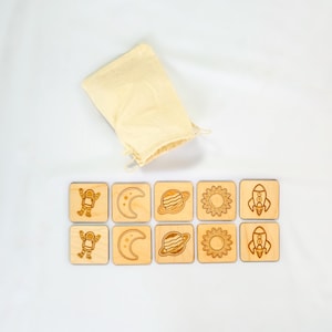 10-piece Montessori space memory match game, five matching pairs of astronaut, crescent moon, Saturn, sun, and rocket wooden tiles on Baltic Birch.  Displayed on white fabric background.