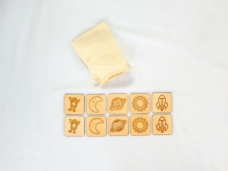 10-piece Montessori space memory match game, five matching pairs of astronaut, crescent moon, Saturn, sun, and rocket wooden tiles on Baltic Birch.  Displayed on white fabric background.