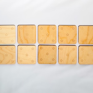 Backs of ten neutral-colored wooden memory match tiles, each engraved with five-star constellation pattern in corners and center of Baltic birch squares.