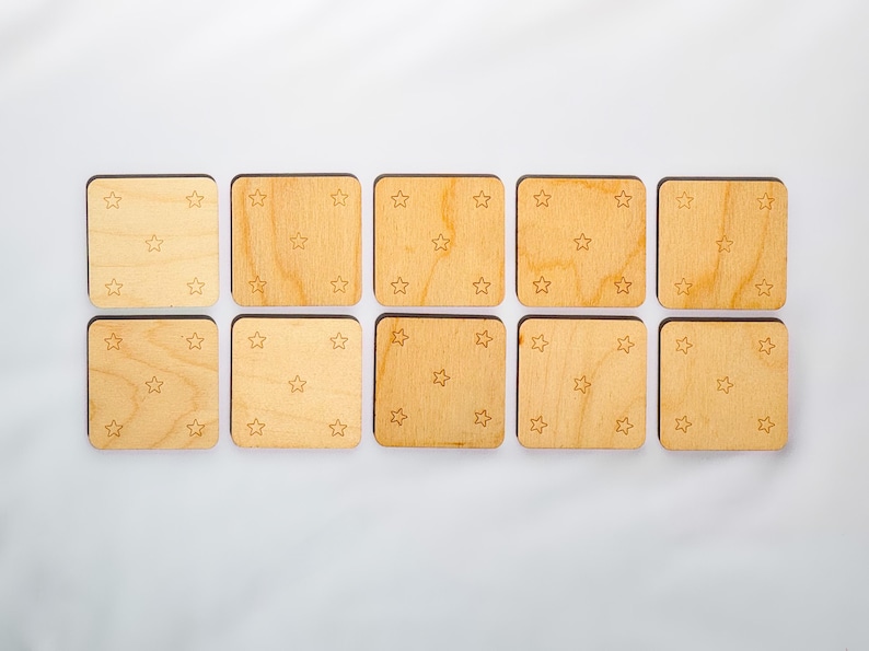 Backs of ten neutral-colored wooden memory match tiles, each engraved with five-star constellation pattern in corners and center of Baltic birch squares.