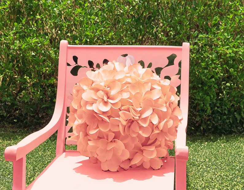 May include: A pink metal chair with a floral cutout design. A large, peach-colored flower sits on the seat of the chair.