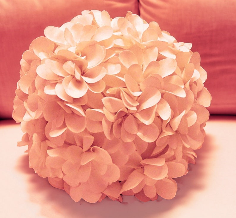 May include: A large, round, peach-colored flower made of fabric petals. The flower is made up of many individual petals that are arranged in a circular pattern.