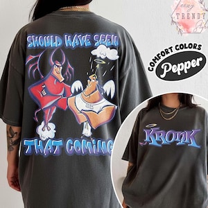 May include: Dark gray t-shirt featuring a cartoon graphic of a devil and an angel. The text "SHOULD HAVE SEEN THAT COMING" is above the characters. The word "KRONK" is on the front of the shirt. The shirt is labeled "COMFORT COLORS Pepper".