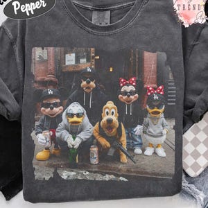 May include: A charcoal gray crewneck t-shirt featuring a graphic print of cartoon characters wearing black baseball caps, sunglasses, and hoodies. The characters are posed in an urban setting, with some holding bottles and one holding a rifle.
