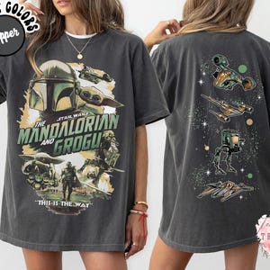 K&ouml;nnte beinhalten: Ein anthrazitfarbenes Kurzarm-T-Shirt mit einem Frontdruck von The Mandalorian und Grogu sowie dem Text "The Mandalorian and Grogu" und "This is the way". Die R&uuml;ckseite zeigt verschiedene Star Wars-Raumschiffe und ein L&auml;ufer-Fahrzeug.
