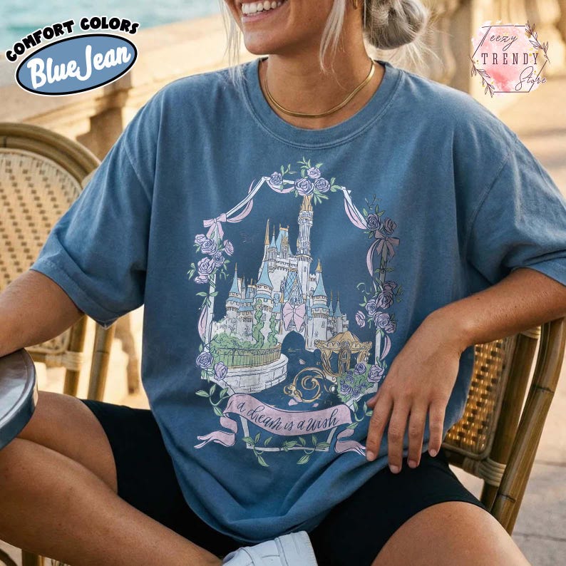 Puede incluir: Camiseta Comfort Colors azul vaquero con un gr&aacute;fico de castillo dentro de una corona floral. El gr&aacute;fico incluye el texto "a dream is a wish". La camiseta tiene mangas cortas y un corte holgado.