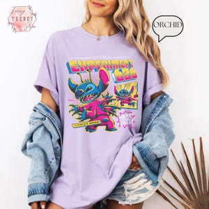 Pode incluir: Uma camiseta lil&aacute;s com um gr&aacute;fico de Stitch de Lilo & Stitch. O design inclui o texto "Stitch Experiment 626" em uma fonte retr&ocirc;, juntamente com as frases "A Complete Mayhem!" e "Hear the All!".