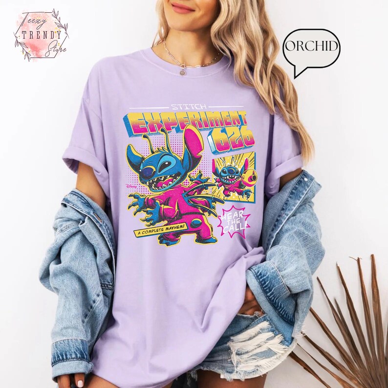 Pode incluir: Uma camiseta lil&aacute;s com um gr&aacute;fico de Stitch de Lilo & Stitch. O design inclui o texto "Stitch Experiment 626" em uma fonte retr&ocirc;, juntamente com as frases "A Complete Mayhem!" e "Hear the All!".