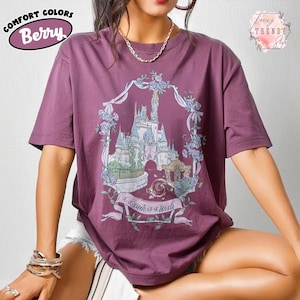 Puede incluir: Camiseta color bayas con un gr&aacute;fico de un castillo dentro de una corona floral. El texto "a dream is a wish" est&aacute; en una pancarta debajo del castillo. La camiseta tiene mangas cortas y cuello redondo. Las palabras "Comfort Colors" y "Berry" est&aacute;n impresas arriba a la izquierda.
