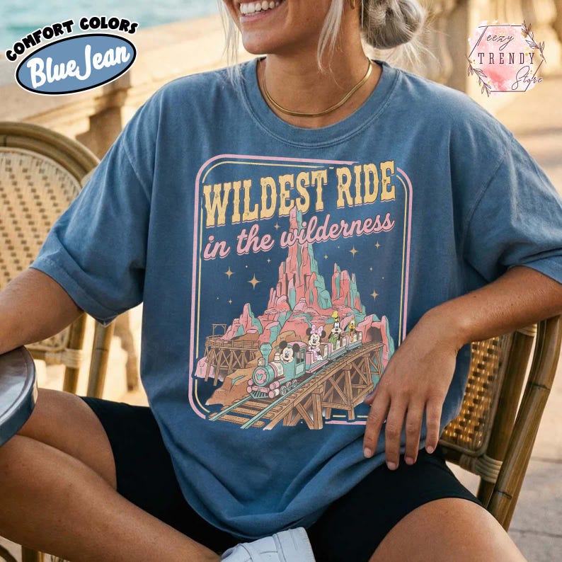 Może przedstawiać: Niebieska koszulka z napisem "WILDEST RIDE in the wilderness" i grafiką pociągu na drewnianym moście, g&oacute;rach i postaciach. Koszulka ma logo Comfort Colors i Blue Jean.