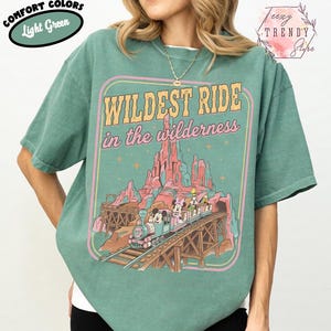 Może przedstawiać: Jasnozielona koszulka z grafiką z napisem &bdquo;Wildest Ride in the wilderness&rdquo;. Grafika przedstawia pociąg z postaciami z kresk&oacute;wek, pasmo g&oacute;rskie i drewniany most. Na koszulce znajdują się r&oacute;wnież słowa &bdquo;Comfort Colors&rdquo; i &bdquo;Light Green&rdquo;.