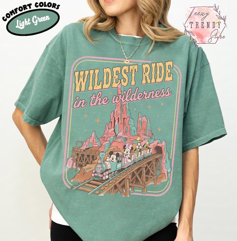 Może przedstawiać: Jasnozielona koszulka z grafiką z napisem &bdquo;Wildest Ride in the wilderness&rdquo;. Grafika przedstawia pociąg z postaciami z kresk&oacute;wek, pasmo g&oacute;rskie i drewniany most. Na koszulce znajdują się r&oacute;wnież słowa &bdquo;Comfort Colors&rdquo; i &bdquo;Light Green&rdquo;.