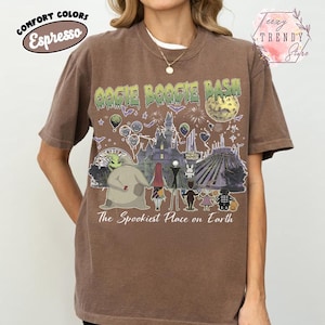 May include: A brown short-sleeve t-shirt featuring a graphic print with the text Oogie Boogie Bash and The Spookiest Place on Earth. The design includes illustrations of characters, a haunted mansion, a moon, and various festive elements.