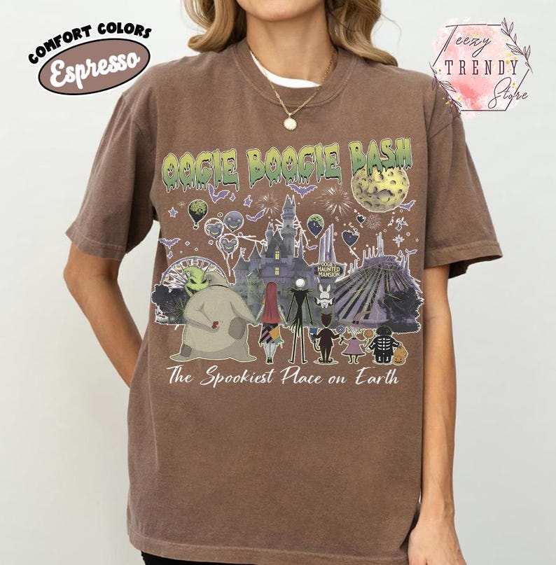 May include: A brown short-sleeve t-shirt featuring a graphic print with the text Oogie Boogie Bash and The Spookiest Place on Earth. The design includes illustrations of characters, a haunted mansion, a moon, and various festive elements.