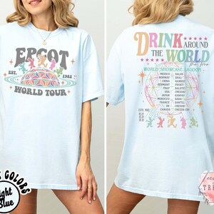 May include: Light blue t-shirt with "EPCOT World Tour" graphic on the front and "Drink Around The World" design on the back. The front graphic features a retro design with the EPCOT logo and the year 1982. The back lists countries.