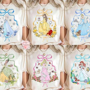 Peut inclure: T-shirts blanc cass&eacute; avec des illustrations &agrave; l'aquarelle de princesses Disney. Chaque t-shirt pr&eacute;sente une princesse diff&eacute;rente dans un cadre d&eacute;coratif avec un n&oelig;ud en haut. Les princesses sont Elsa, Belle, Cendrillon, Tiana, Aurore et Ariel.