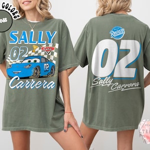 May include: Moss green t-shirt featuring a blue race car graphic with the text "SALLY 02 Carrera" on the front. The back of the shirt displays a large "02" and "Sally Carrera" text. The shirt has a relaxed fit.
