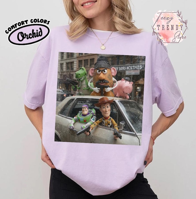 Puede incluir: Una camiseta de color morado claro con un estampado gr&aacute;fico de personajes de Toy Story, incluidos Buzz Lightyear, Woody, el Sr. Patata, Rex y Hamm. Los personajes aparecen en un estilo cinematogr&aacute;fico, algunos con pistolas de juguete, alrededor y dentro de un coche.