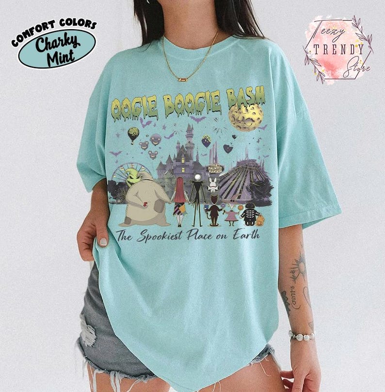 May include: A light mint green t-shirt featuring a graphic print with the text Oogie Boogie Bash and The Spookiest Place on Earth. The design includes characters from The Nightmare Before Christmas, a castle, a moon, and various park attractions.