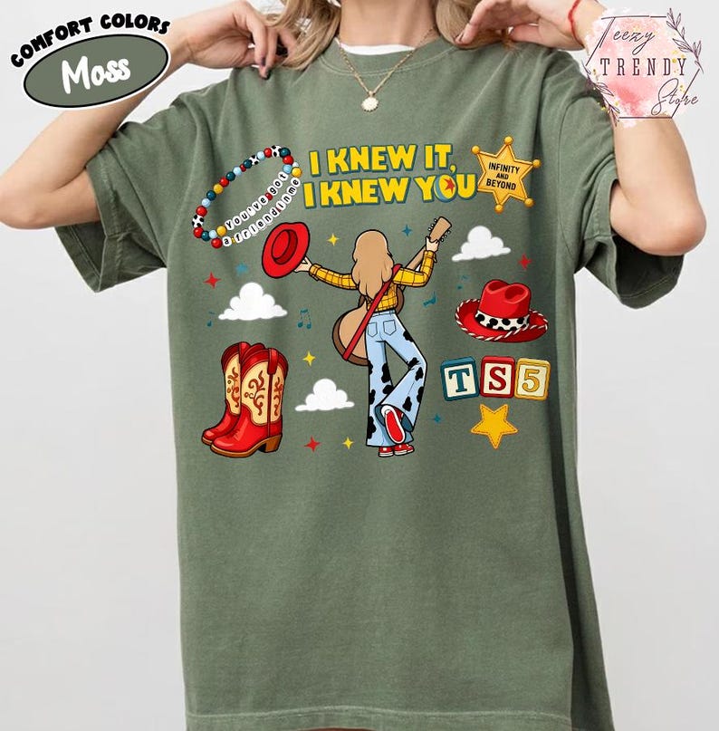 May include: A moss green t-shirt featuring a graphic print with the text I KNEW IT, I KNEW YOU, a character playing a guitar, a beaded bracelet, a red cowboy hat, red cowboy boots, a sheriff badge, clouds, stars, and the text TS5.