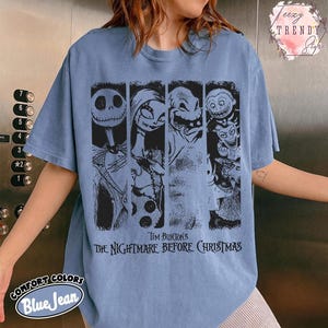 May include: A blue jean coloured t-shirt featuring a black graphic print of characters from Tim Burton's The Nightmare Before Christmas. The design includes four vertical panels showing Jack Skellington, Sally, Oogie Boogie, and Lock, Shock, and Barrel.