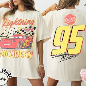 May include: Ivory-colored t-shirt featuring a graphic of Lightning McQueen race car with the number 95. The front design includes the text "Lightning McQueen" and "MCQUEEN". The back of the shirt displays a large number 95 and the text "Lightning McQueen".