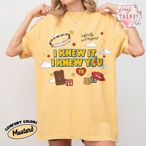 Puede incluir: Una camiseta color amarillo mostaza con un estampado gr&aacute;fico que incluye el texto I KNEW IT, I KNEW YOU, infinity and beyond, y YOU'VE GOT A FRIEND IN ME. El dise&ntilde;o presenta ilustraciones de botas vaqueras, un sombrero rojo, cubos y estrellas.