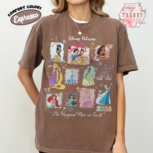 May include: Brown t-shirt featuring Disney Princesses in framed illustrations. The shirt includes the text "Disney Princess" and "2026". The phrase "The Happiest Place on Earth" is also printed on the shirt.