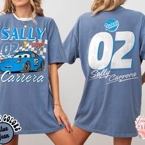May include: A blue jean-colored t-shirt featuring the character Sally Carrera from the movie Cars. The front graphic includes the text "SALLY 02 Carrera" with a cartoon image of the car. The back of the shirt displays "02 Sally Carrera".