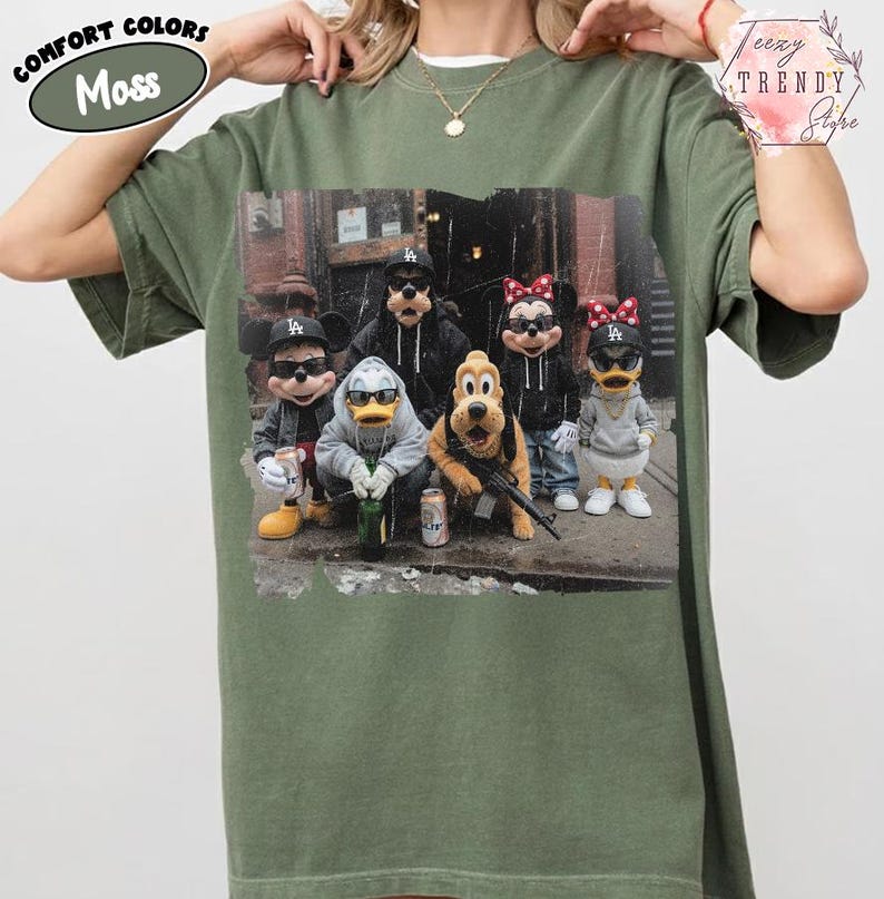 May include: A moss green short-sleeve t-shirt featuring a graphic print of five cartoon characters wearing black baseball caps and sunglasses. The characters are dressed in casual streetwear, including hoodies and jackets, and are posed together in an urban setting.