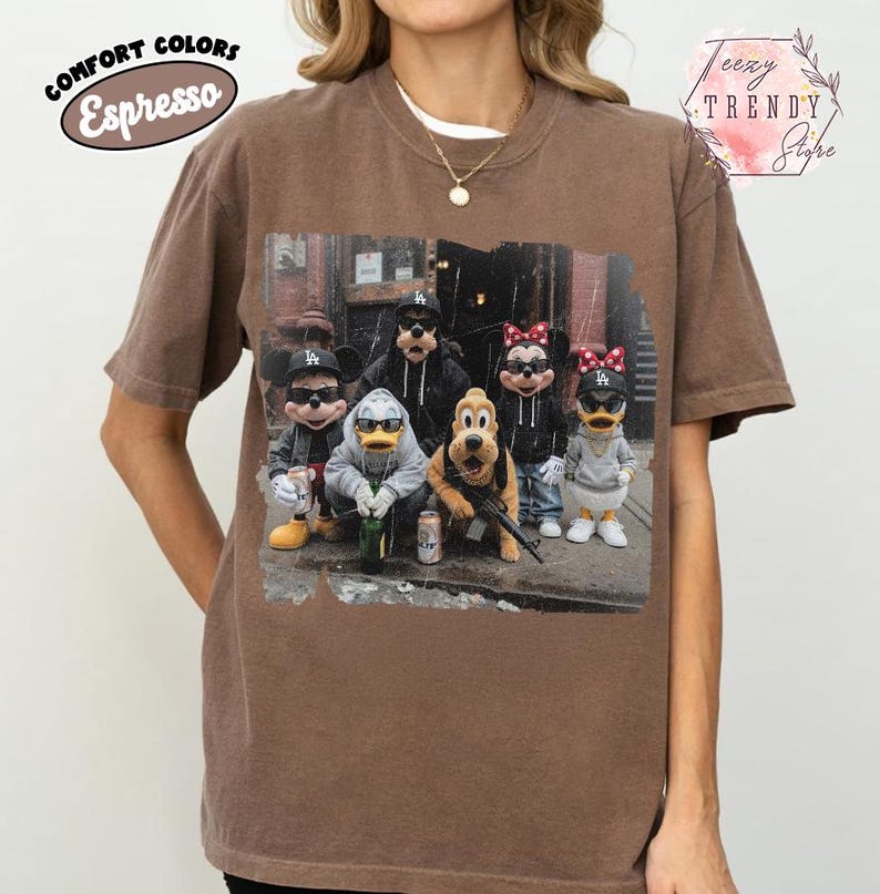 May include: A brown short-sleeve t-shirt featuring a graphic print of five cartoon characters wearing Los Angeles Dodgers baseball caps and casual clothing. The print shows Mickey Mouse, Donald Duck, Goofy, Pluto, and Minnie Mouse in an urban setting.