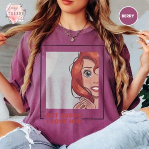 Puede incluir: Camiseta color bayas con un personaje de dibujos animados de pelo rojo y ojos azules. El texto "BUT DADDY I LOVE HIM" est&aacute; debajo del gr&aacute;fico. La camiseta tiene cuello redondo y mangas cortas. La camiseta es de corte holgado.