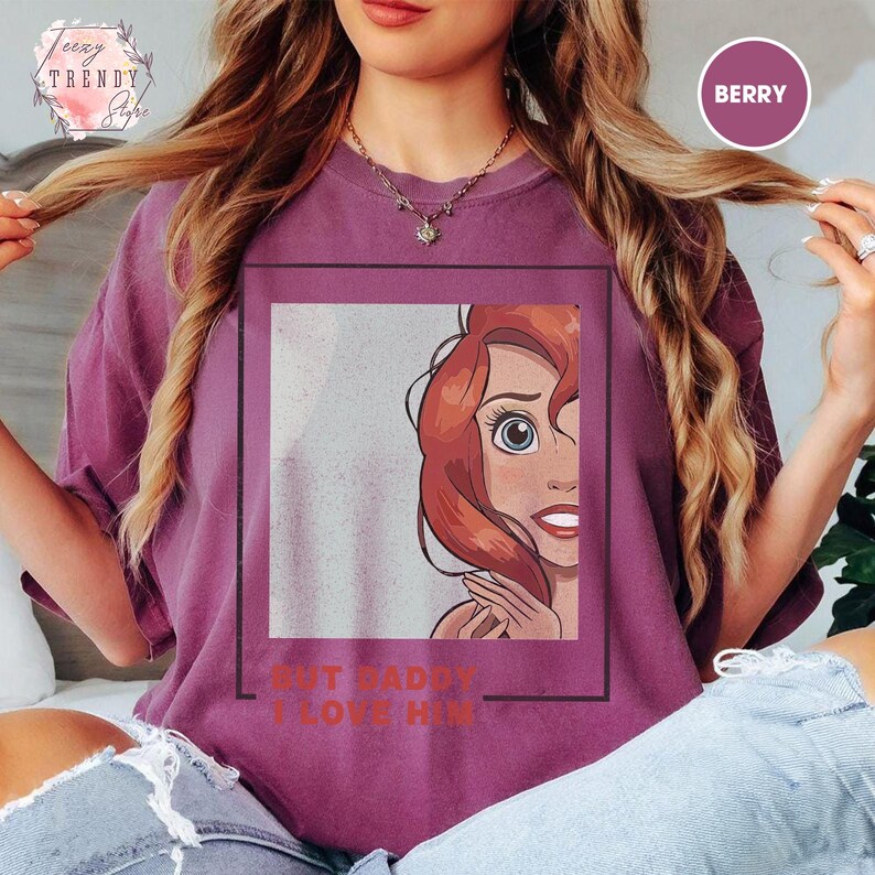 Puede incluir: Camiseta color bayas con un personaje de dibujos animados de pelo rojo y ojos azules. El texto "BUT DADDY I LOVE HIM" est&aacute; debajo del gr&aacute;fico. La camiseta tiene cuello redondo y mangas cortas. La camiseta es de corte holgado.