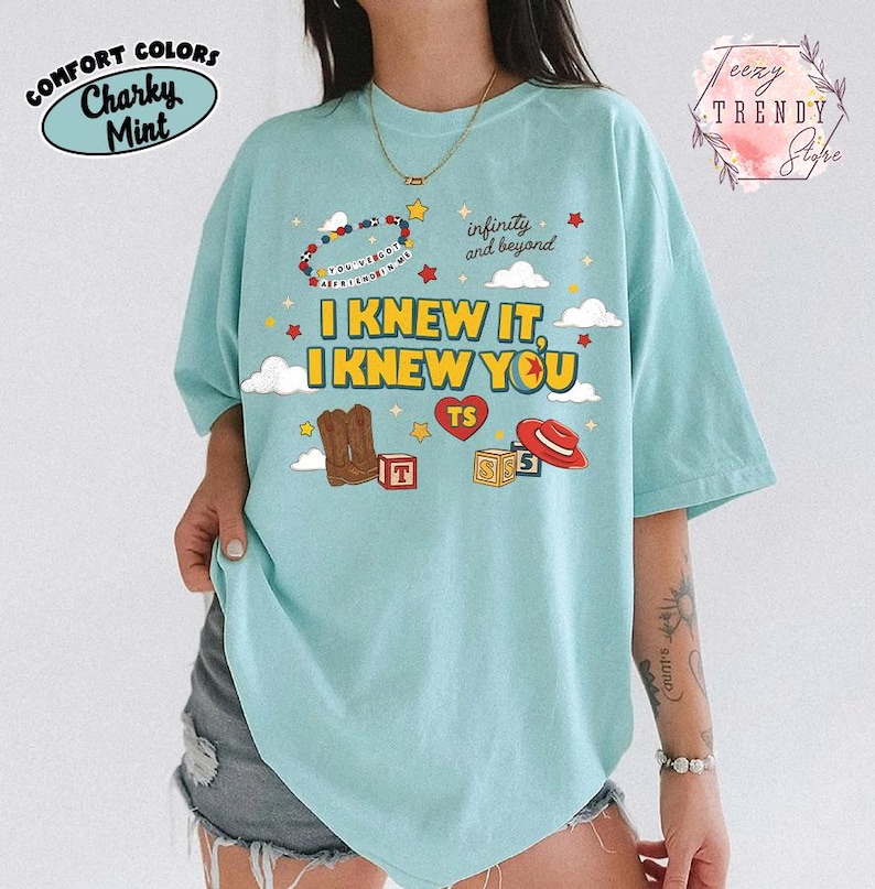 Puede incluir: Una camiseta de color verde menta claro con un estampado gr&aacute;fico que incluye el texto I KNEW IT, I KNEW YOU, infinity and beyond y YOU'VE GOT A FRIEND IN ME. El dise&ntilde;o presenta ilustraciones de botas vaqueras, un sombrero rojo, bloques y estrellas.