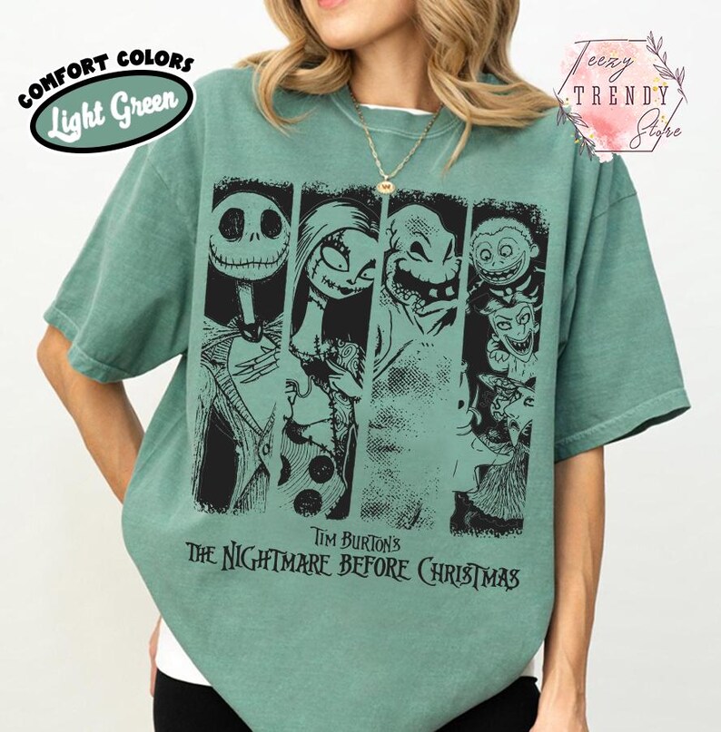 May include: A light green short-sleeve t-shirt featuring a black graphic print of characters from Tim Burton's The Nightmare Before Christmas. The design includes Jack Skellington, Sally, Oogie Boogie, and other figures arranged in vertical panels.