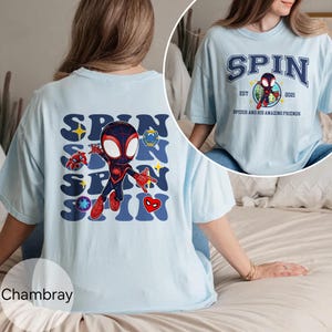 Puede incluir: Camiseta azul claro con un gr&aacute;fico de dibujos animados de un superh&eacute;roe y la palabra "SPIN". La parte posterior de la camiseta tiene una versi&oacute;n m&aacute;s grande del mismo dise&ntilde;o. La camiseta tambi&eacute;n tiene el texto "SPIDER AND HIS AMAZING FRIENDS".