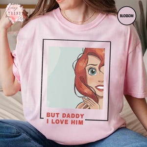 Puede incluir: Camiseta rosa claro con una ilustraci&oacute;n de dibujos animados de un personaje con cabello rojo y ojos azules. El texto "BUT DADDY I LOVE HIM" est&aacute; impreso en rojo. La camiseta tiene cuello redondo y mangas cortas.