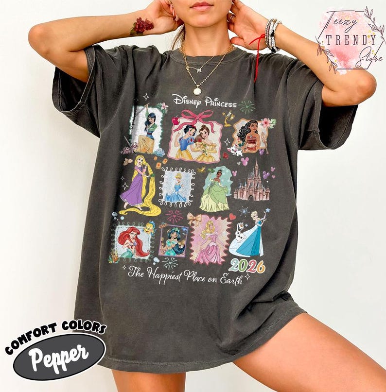 May include: Dark gray t-shirt featuring Disney Princesses in a collage design. The shirt includes the text "Disney Princess" and "The Happiest Place on Earth 2026". The shirt is a Comfort Colors Pepper tee.