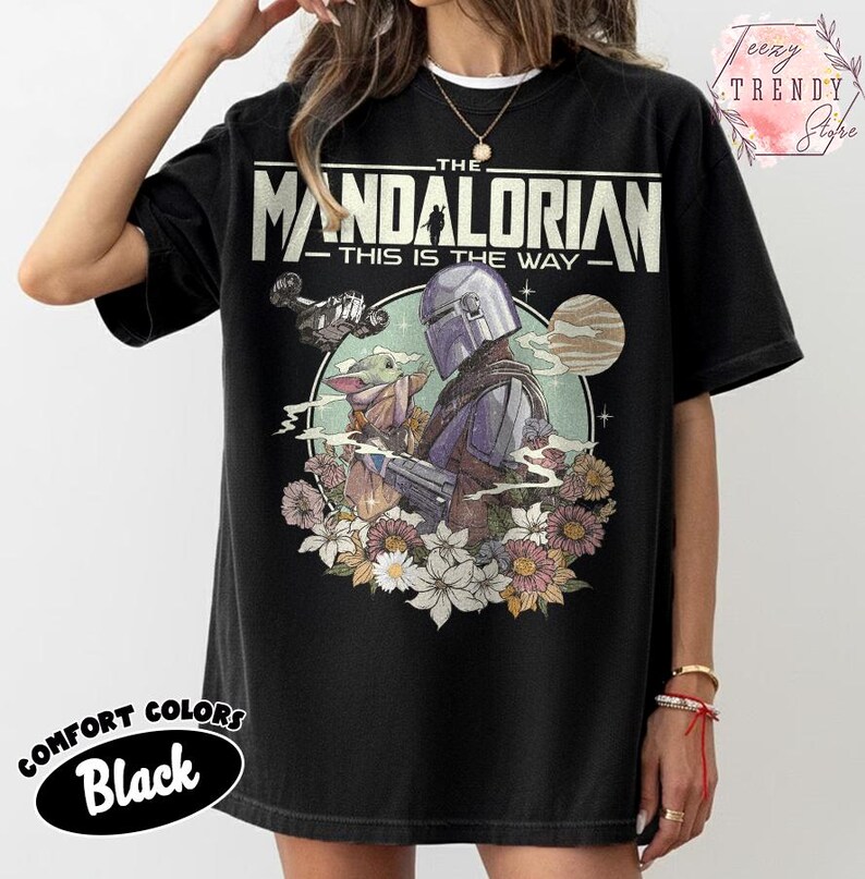 May include: Black t-shirt with a graphic of The Mandalorian and Grogu, floral elements, and the text "THE MANDALORIAN - THIS IS THE WAY." Made from Comfort Colors material.