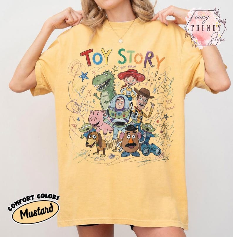 May include: Mustard yellow t-shirt featuring a colorful graphic of Toy Story characters. The text "Toy Story" is above the characters. The shirt has a crew neck and short sleeves. The words "Comfort Colors" and "Mustard" are printed on the bottom left.