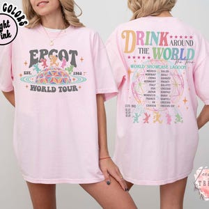 May include: Light pink t-shirt with "EPCOT World Tour" graphic on the front and "Drink Around The World" design on the back. The front graphic features a colorful geometric sphere and characters. The back design lists countries.