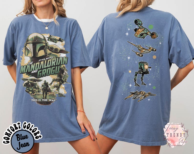 K&ouml;nnte beinhalten: Ein blaues T-Shirt mit einer Grafik auf der Vorderseite, die The Mandalorian und Grogu zeigt, zusammen mit dem Text "The Mandalorian and Grogu" und "This is the way". Die R&uuml;ckseite zeigt eine vertikale Anordnung von vier Raumschiffen.