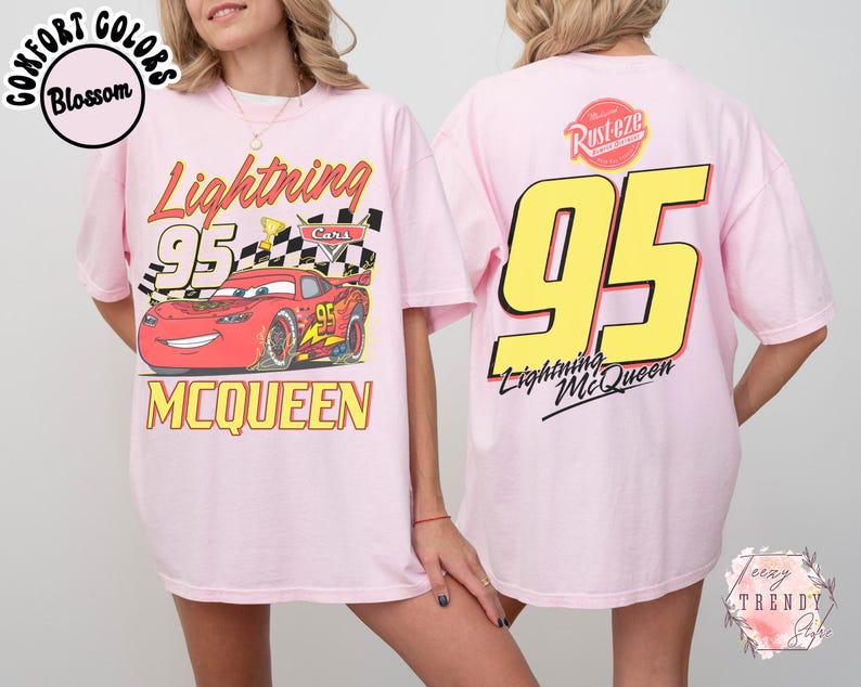 May include: Light pink t-shirt featuring a graphic of Lightning McQueen from the Cars movie. The front of the shirt displays the character with the number 95 and the name McQueen. The back of the shirt has a large yellow 95 and the Lightning McQueen logo.