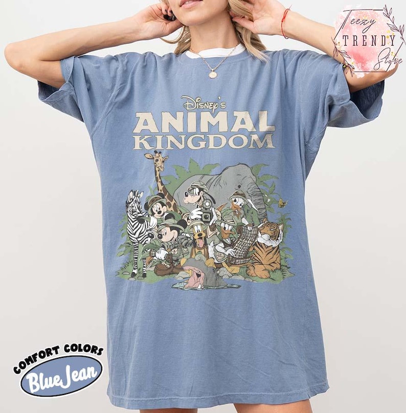 May include: Blue jean coloured t-shirt featuring the text "Disney's Animal Kingdom" above a graphic of Disney characters and animals. The shirt is a Comfort Colors brand.