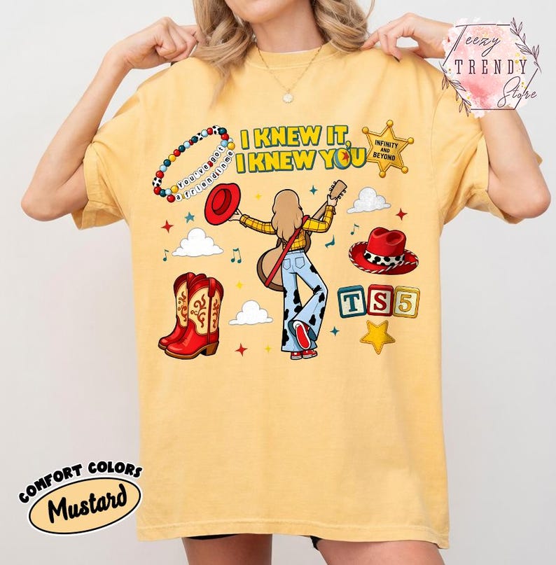 May include: A mustard yellow t-shirt featuring a graphic print with the text I KNEW IT, I KNEW YOU, a beaded bracelet, a sheriff badge, a red hat, a guitar, cowboy boots, and alphabet blocks spelling TS5, surrounded by clouds and stars.