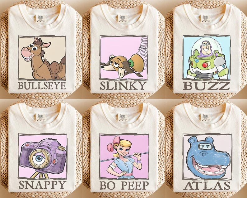May include: Six cream-coloured t-shirts featuring cartoon characters from the Toy Story franchise. Each shirt has a different character: Bullseye, Slinky, Buzz, Snappy, Bo Peep, and Atlas, each in a framed design with their name below.